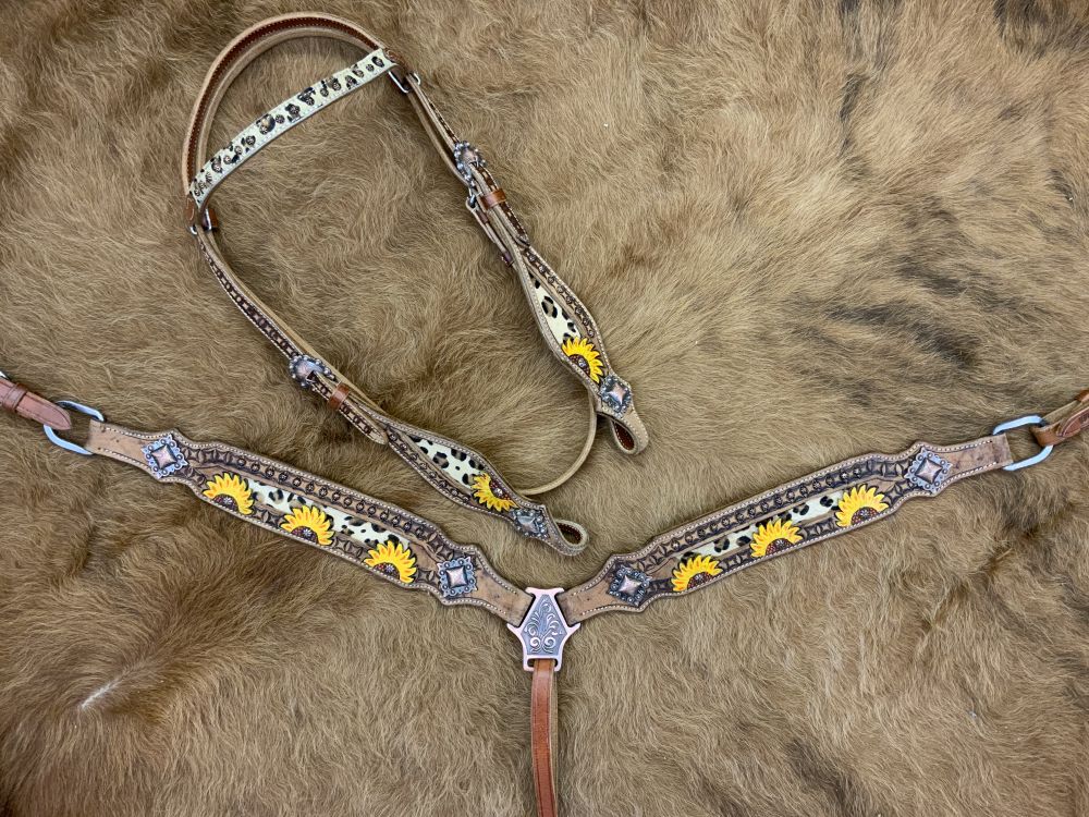 Medium oil western headstall with tooled sunflower leather and cheetah print inlay. Cheetah print lies on browband with copper floral studs. Copper square conchos accent the end of tooling and cheetah inlays. Copper floral concho studs line the tooled leather of breast collar with studs for the middle of the sunflower tooling. Set lays on cowhide rug. 