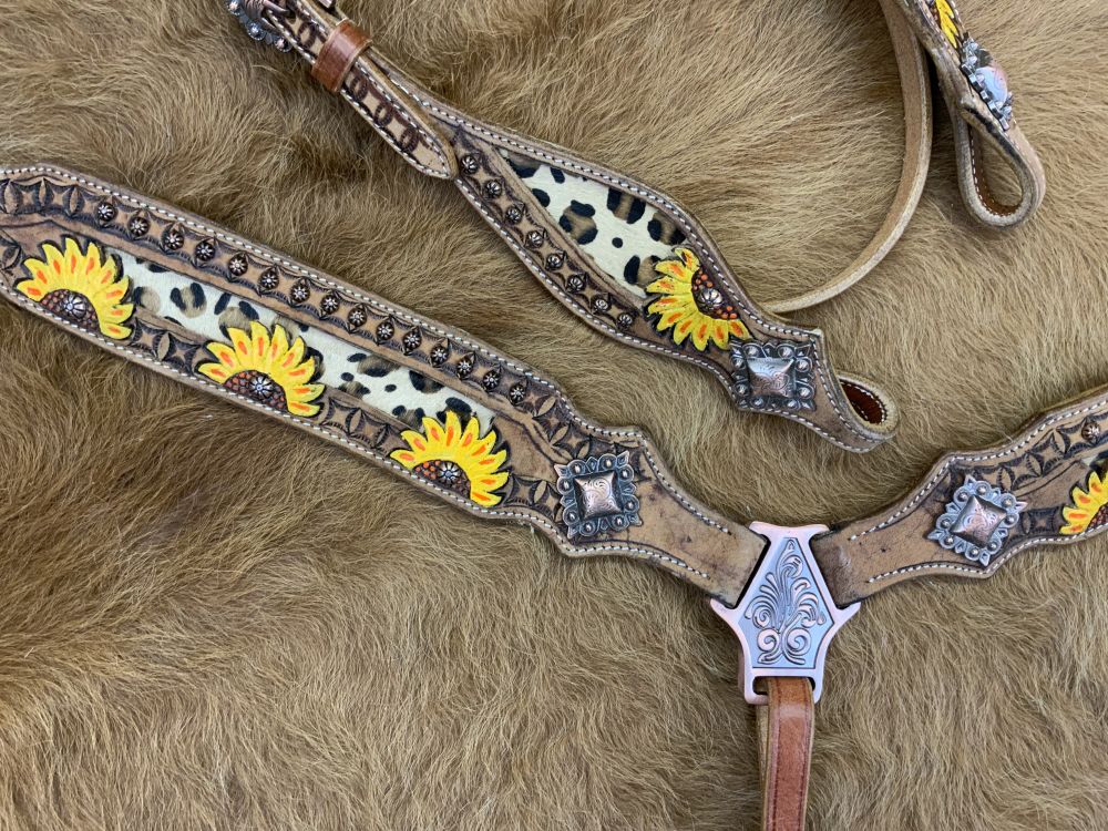Medium oil western headstall with tooled sunflower leather and cheetah print inlay. Cheetah print lies on browband with copper floral studs. Copper square conchos accent the end of tooling and cheetah inlays. Copper floral concho studs line the tooled leather of breast collar with studs for the middle of the sunflower tooling. Zoomed in showing tooling design and conchos. 