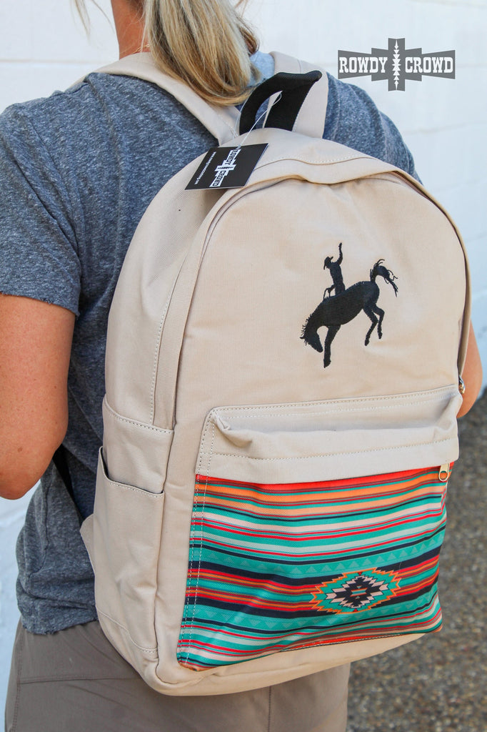 Tan canvas bag with black embroidered buckaroo. Front pocket has southwestern designed canvas accent. Side pockets are visible for water bottles. 