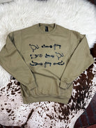 Anbrown crewneck sweatshirt with black western-themed graphic prints, laid flat on a white faux fur rug and a brown and white cowhide rug.