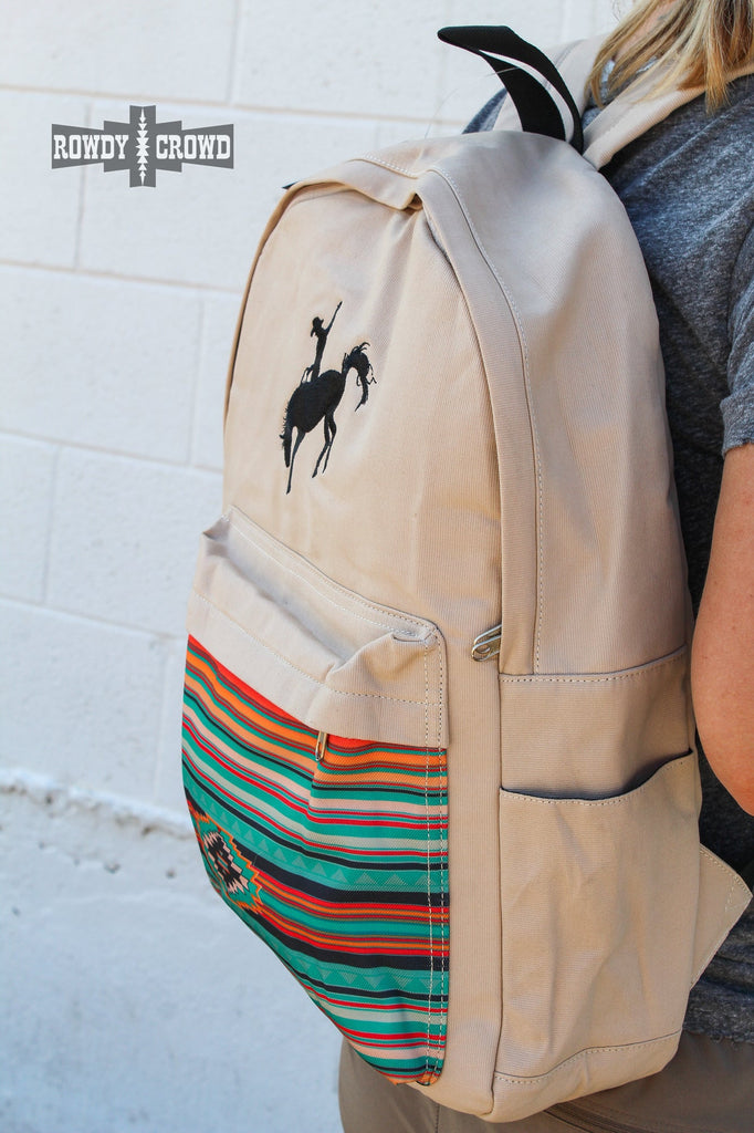 Tan canvas bag with black embroidered buckaroo. Front pocket has southwestern designed canvas accent. Side pockets are visible for water bottles. 