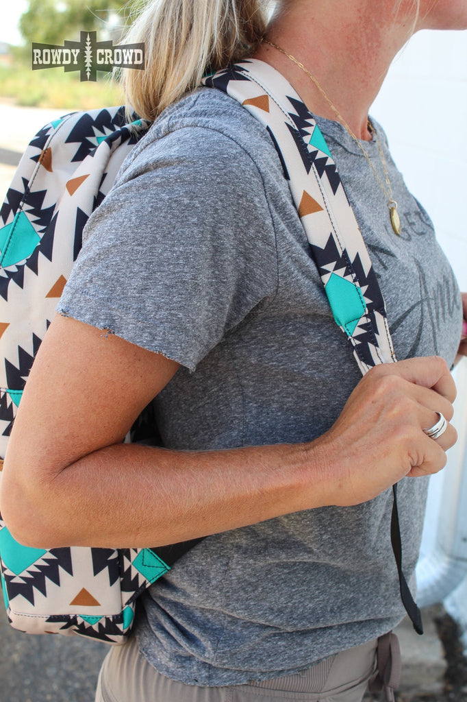 Western backpack with tan canvas and a tribal design with teals and oranges. Black canvas pocket with zipper pocket. Matching canvas for side pockets.  Model pulls on shoulder strap showing how adjustable it is. 