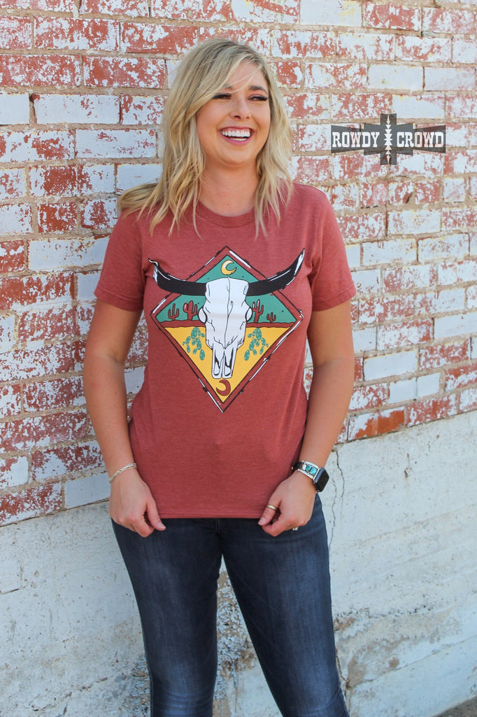 rust colored steer skull western graphic tee with cactus design, model is blonde with dark denim jeans and brick background