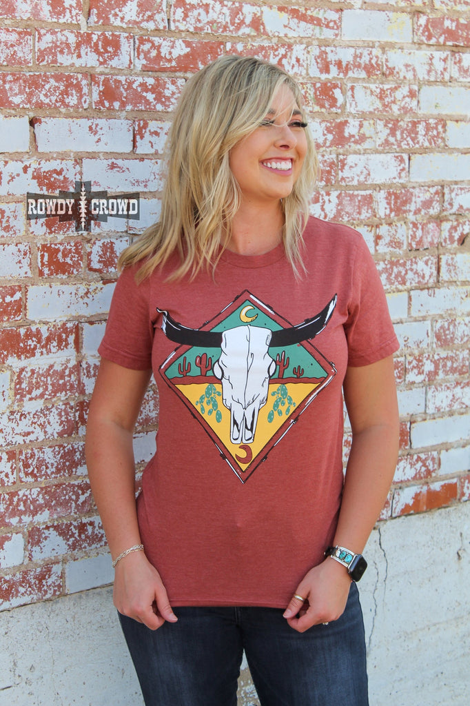 rust colored western graphic tee with steer skull and cactus design, model is wearing denim jeans and brick background