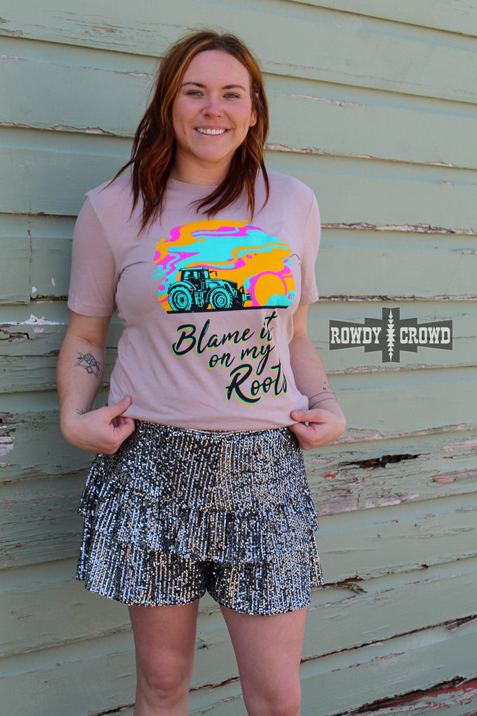 Black sequin shorts with ruffles on model with pink shirt on up against a green wood wall. 
