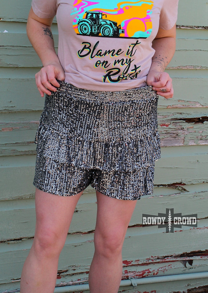 Black sequin shorts on model with pink short on up against a green wood wall. 