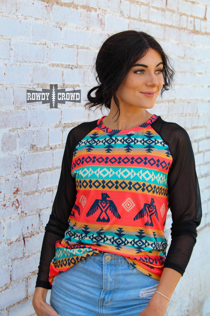 Guadalupe southwestern colorful long sleeve with mesh sleeves. Thunderbirds and aztec designs run along the colorful sectors of the shirt. Model wears this with distressed jeans against a white brick wall.