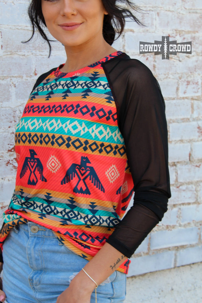 Guadalupe southwestern colorful long sleeve with mesh sleeves. Thunderbirds and aztec designs run along the colorful sectors of the shirt. Model wears this with distressed jeans against a white brick wall.