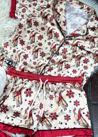 red and cream santa bronc silky pajamas, two piece outfit laid on a white fluffy rug with white slippers 