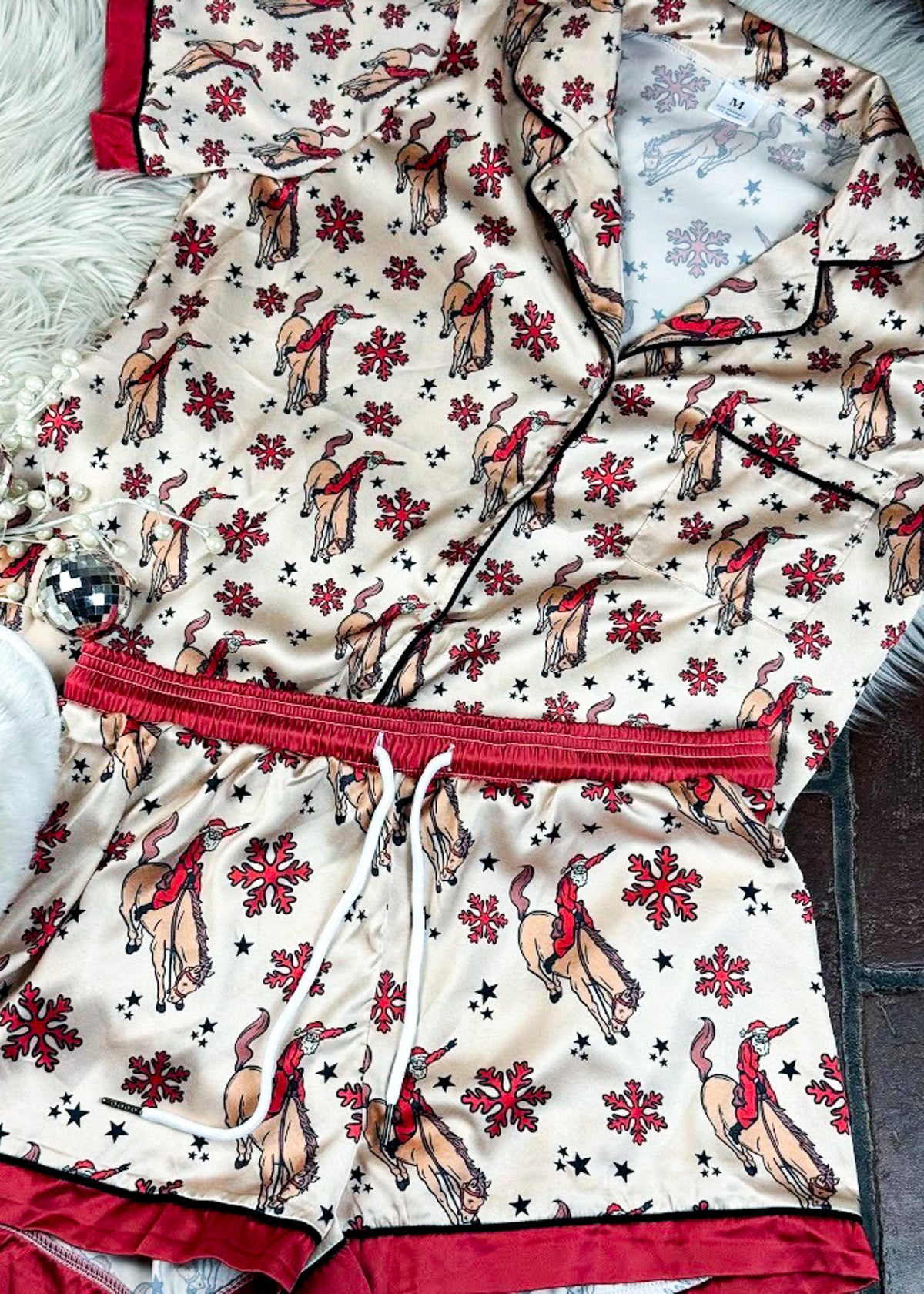 red and cream santa bronc silky pajamas, two piece outfit laid on a white fluffy rug with white slippers 
