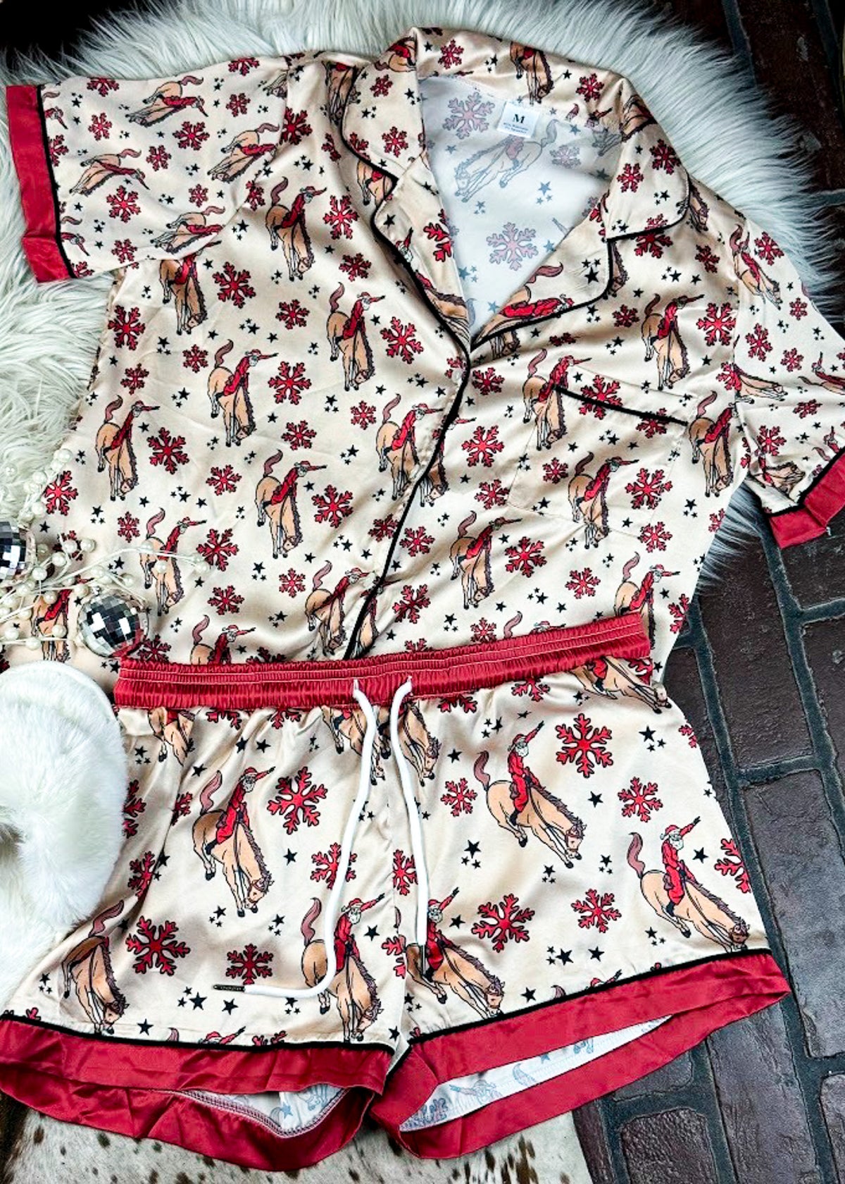 red and cream santa bronc silky pajamas, two piece outfit laid on a white fluffy rug with white slippers 