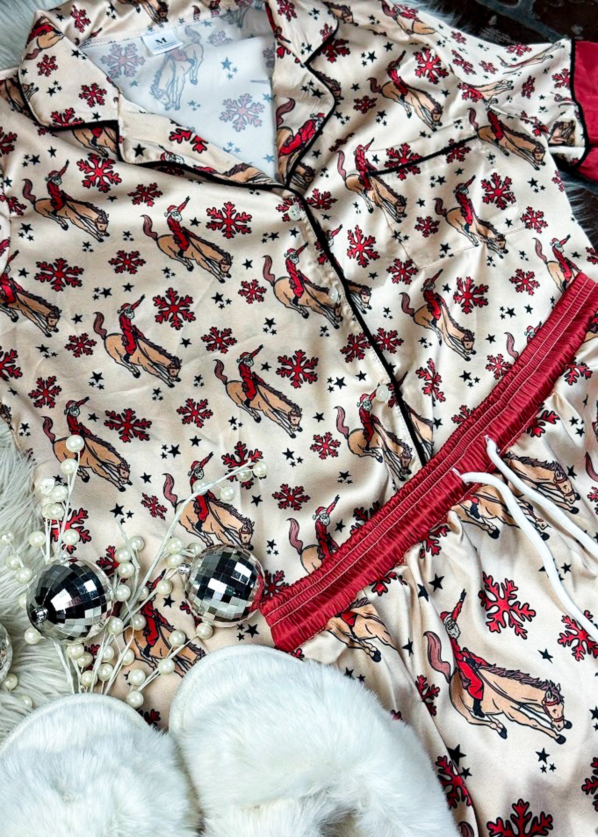 red and cream santa bronc silky pajamas, two piece outfit laid on a white fluffy rug with white slippers 