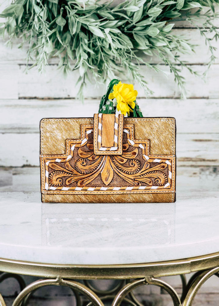 Southwestern Cowhide Buckstitch Wallet pictured on white table with cactus and green decor in the background