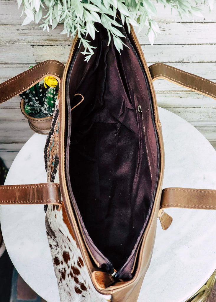 western cowhide tote handbag with teal and floral tooled leather down the center, pictured on white table with green decor