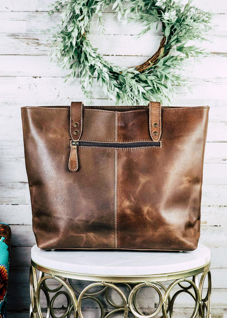 western cowhide tote handbag with teal and floral tooled leather down the center, pictured on white table with green decor