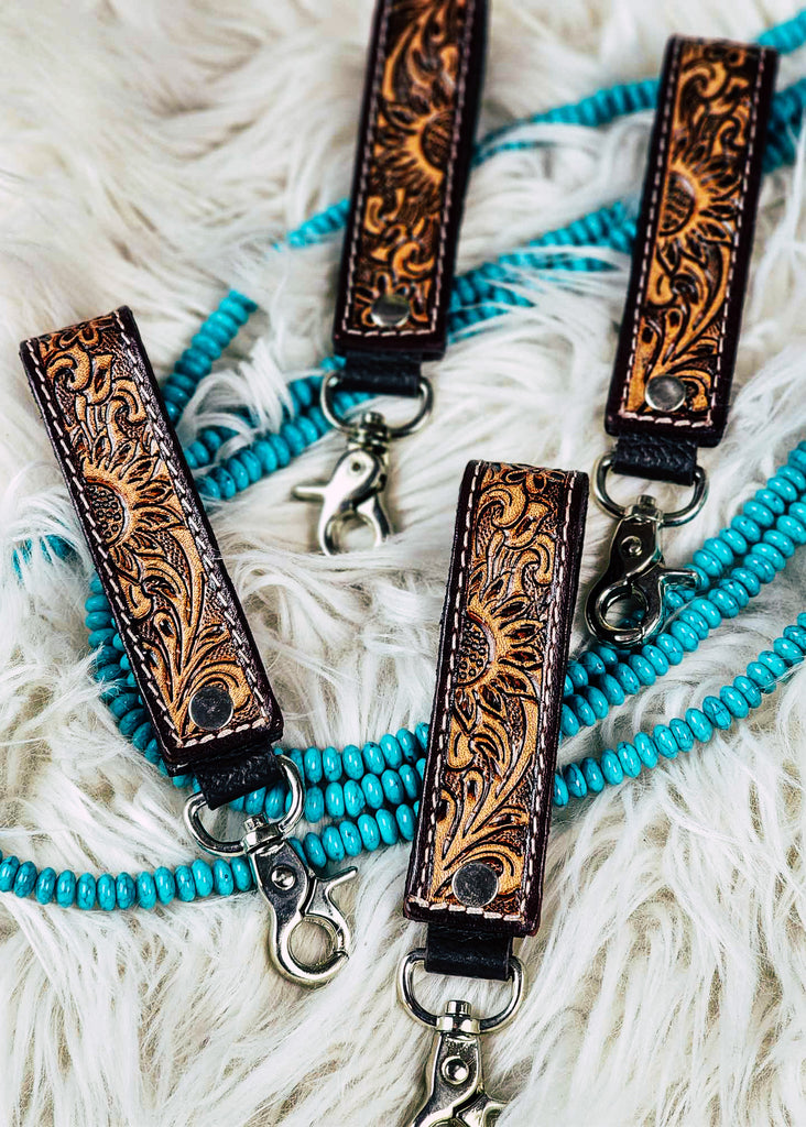 tooled leather sunflower design western keyrings on white rug and turquoise beads