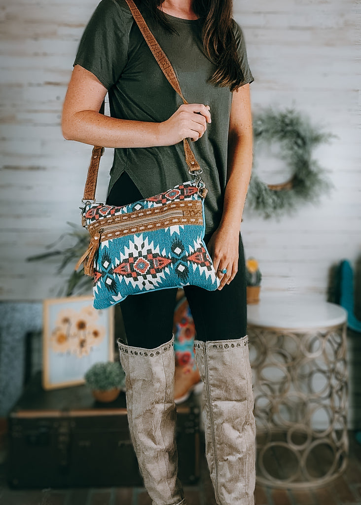 Turquoise Southwest Small Crossbody Bag on model with olive green shirt, black leggings and tan knee high boots with western and farmhouse decor in the background