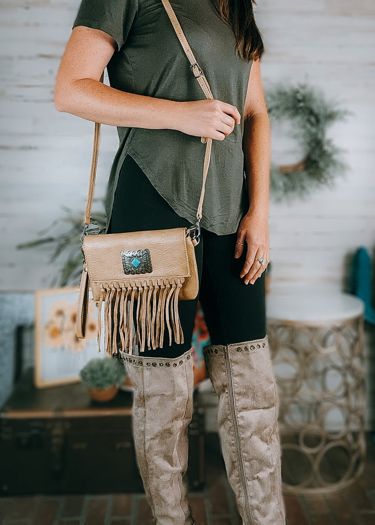 Turquoise Stone Concho Crossbody Clutch on model wearing olive green shirt, black leggings and tan knee high boots. western decor in the background.