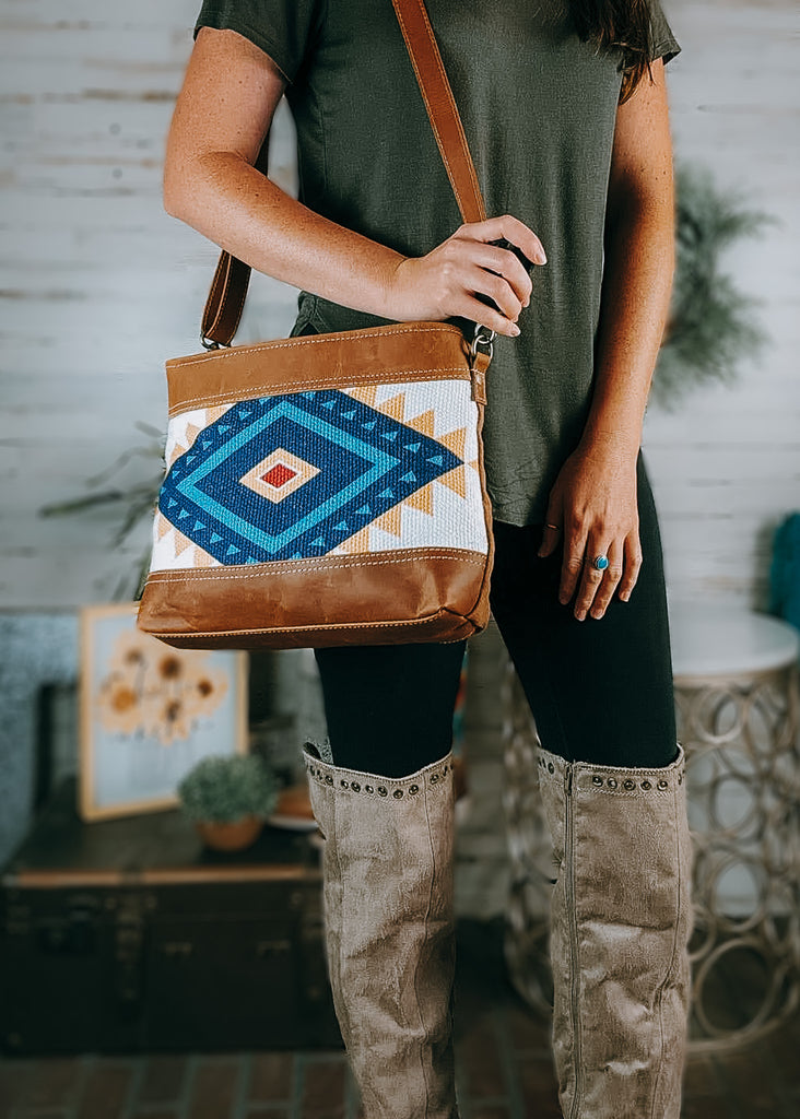 Yellow & Blue Aztec Crossbody Handbag on model wearing olive green shirt, black leggings and tan knee high boots, background has western and farmhouse decor