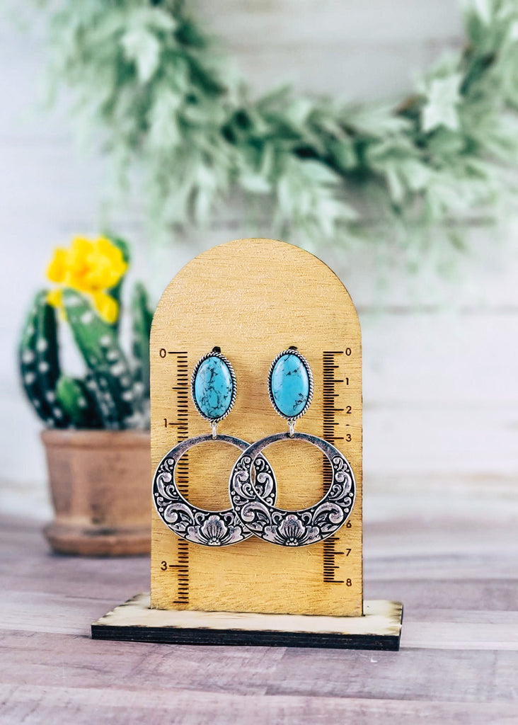 Turquoise Hoop Earrings on wood background with green decor in corner hanging on measurement stand