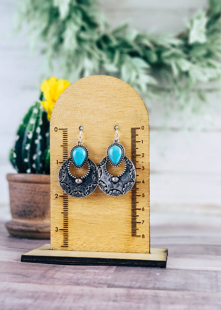 Turquoise & Silver Round Southwestern Earrings on wood background with green decor hanging on mesurement stand
