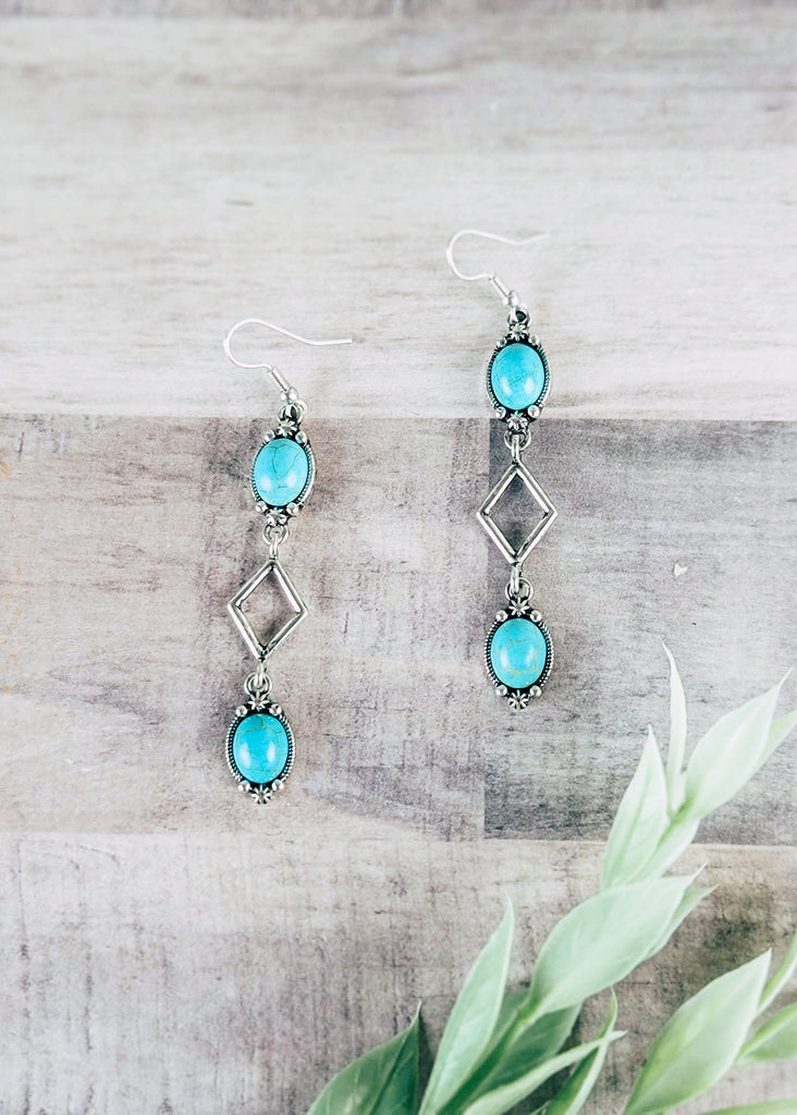 Dangle Turquoise Earrings on wood background with green decor