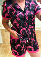 A person wearing a short-sleeve pajama romper with a black and pink floral print, standing in a tiled bathroom setting.