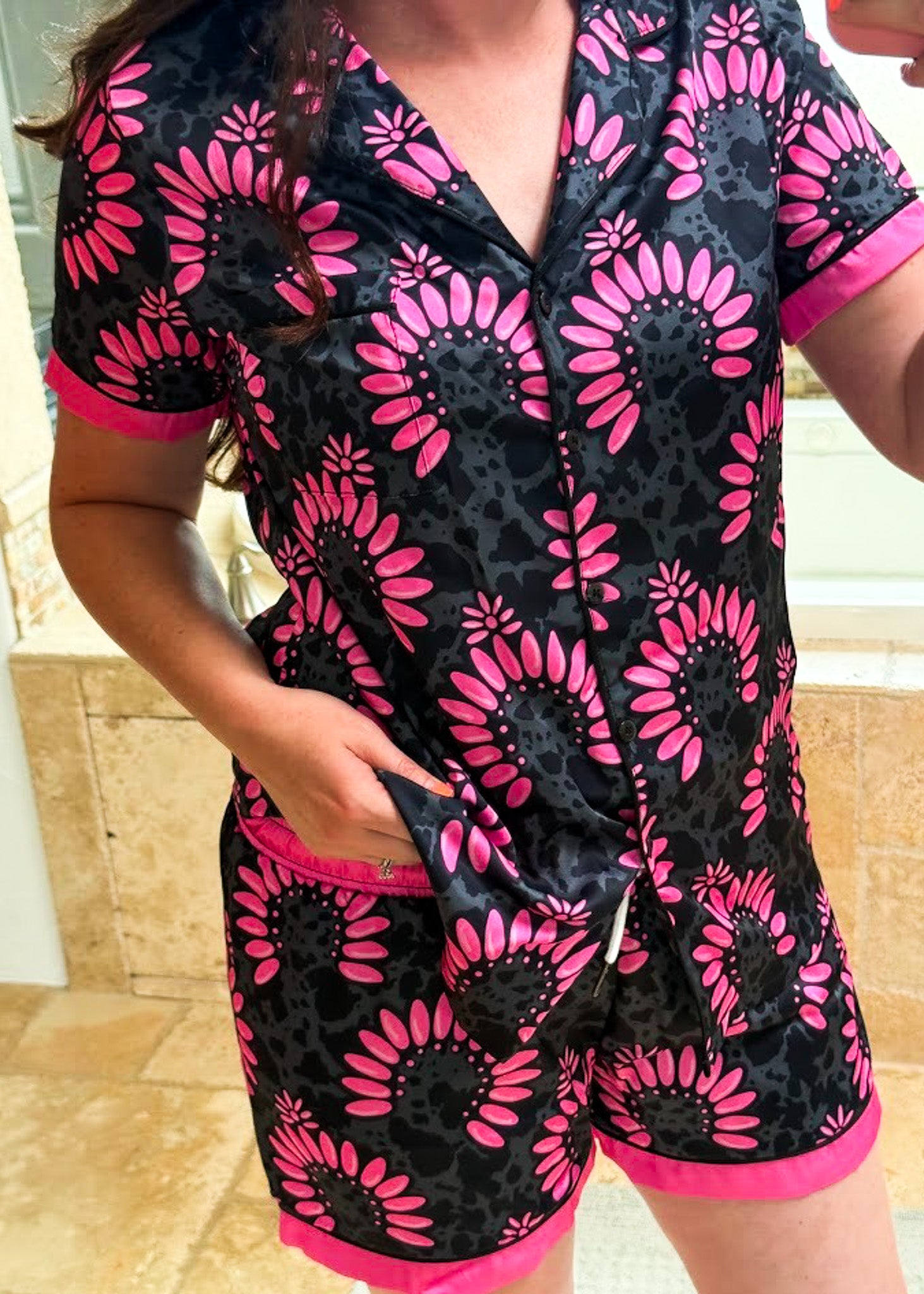 A person wearing a short-sleeve pajama romper with a black and pink floral print, standing in a tiled bathroom setting.