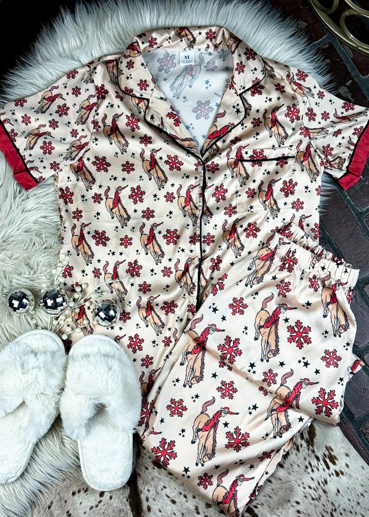 red and cream santa bronc silky pajamas laying on a white fluffy rug with white slippers and disco ball decor 