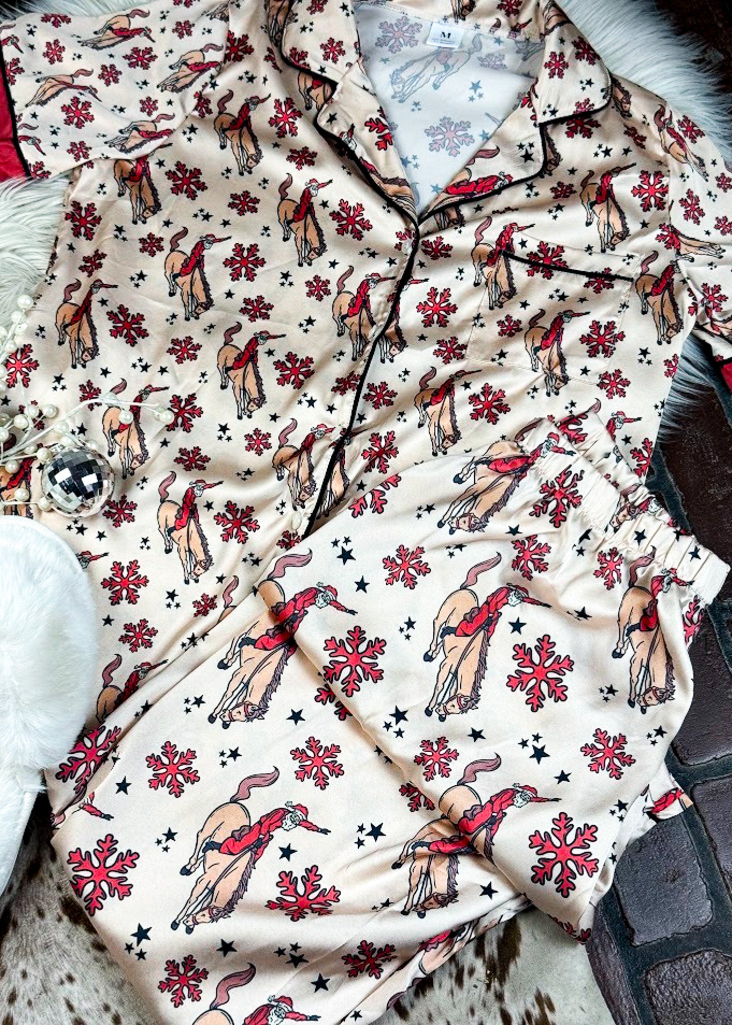red and cream santa bronc silky pajamas laying on a white fluffy rug with white slippers and disco ball decor 