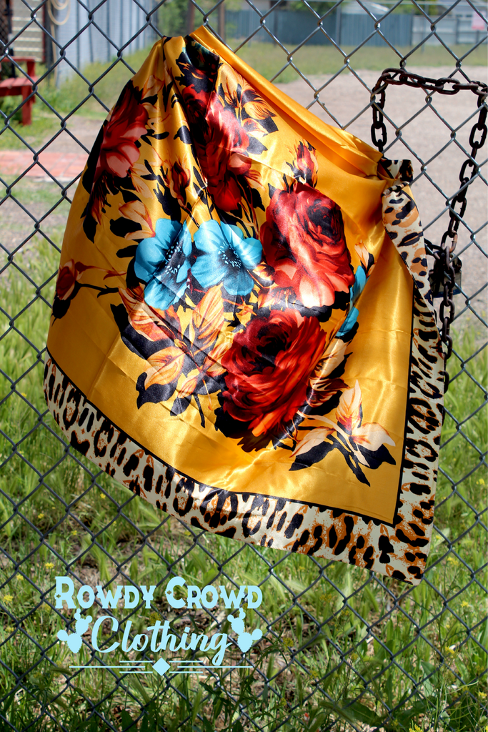 Fiesty floral wild rag with leopard print boarders and yellow main colors. Pops of color are added with the floral print. Wild rag hang from a chain link fence.