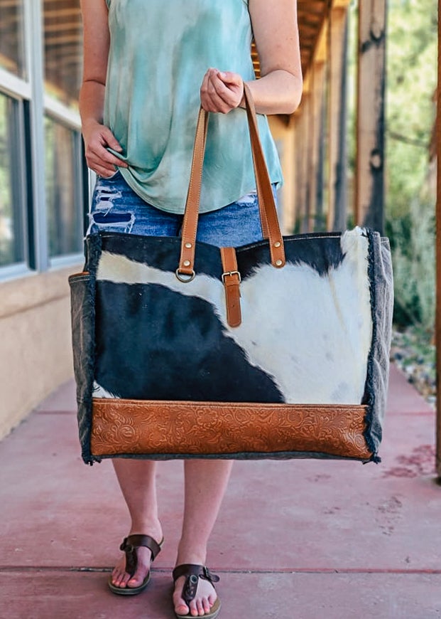 Cowhide with bottom floral tooled paneling. Matching straps and buckle. Frayed edges on the side with a side open pocket. 