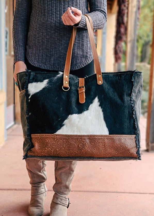 Cowhide with bottom floral tooled paneling. Matching straps and buckle. Frayed edges on the side with a side open pocket.  Style B