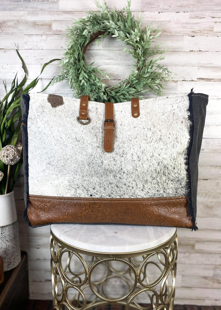 Black & White Cowhide Floral Tooled Weekender Bag [Style C] on white table with green floral decor