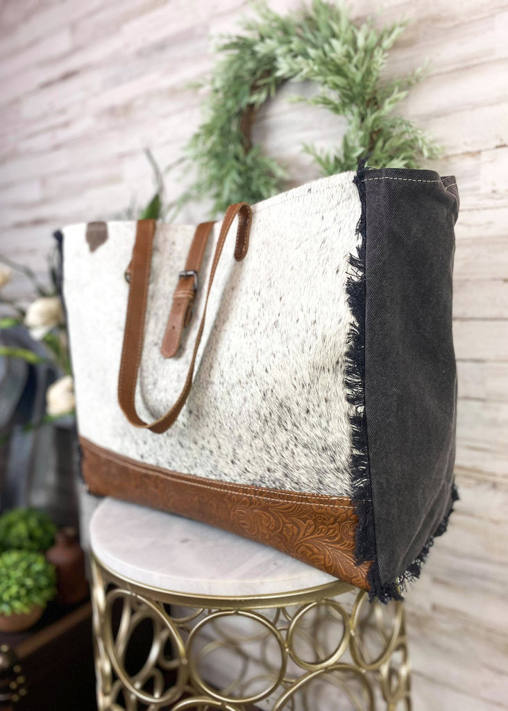 Black & White Cowhide Floral Tooled Weekender Bag [Style C] on white table with green floral decor