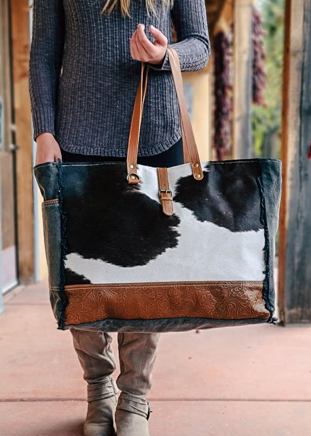 Cowhide with bottom floral tooled paneling. Matching straps and buckle. Frayed edges on the side with a side open pocket. Style D