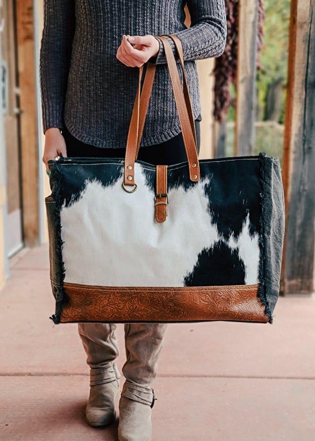 Cowhide with bottom floral tooled paneling. Matching straps and buckle. Frayed edges on the side with a side open pocket. Model holds this on her arm. 