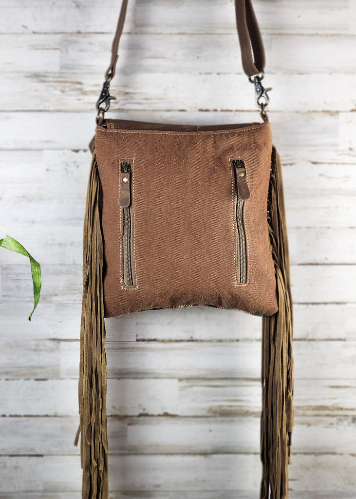 Backside brown canvas bag with two zippered to a concealed pocket. Fringe hags from the side. 
