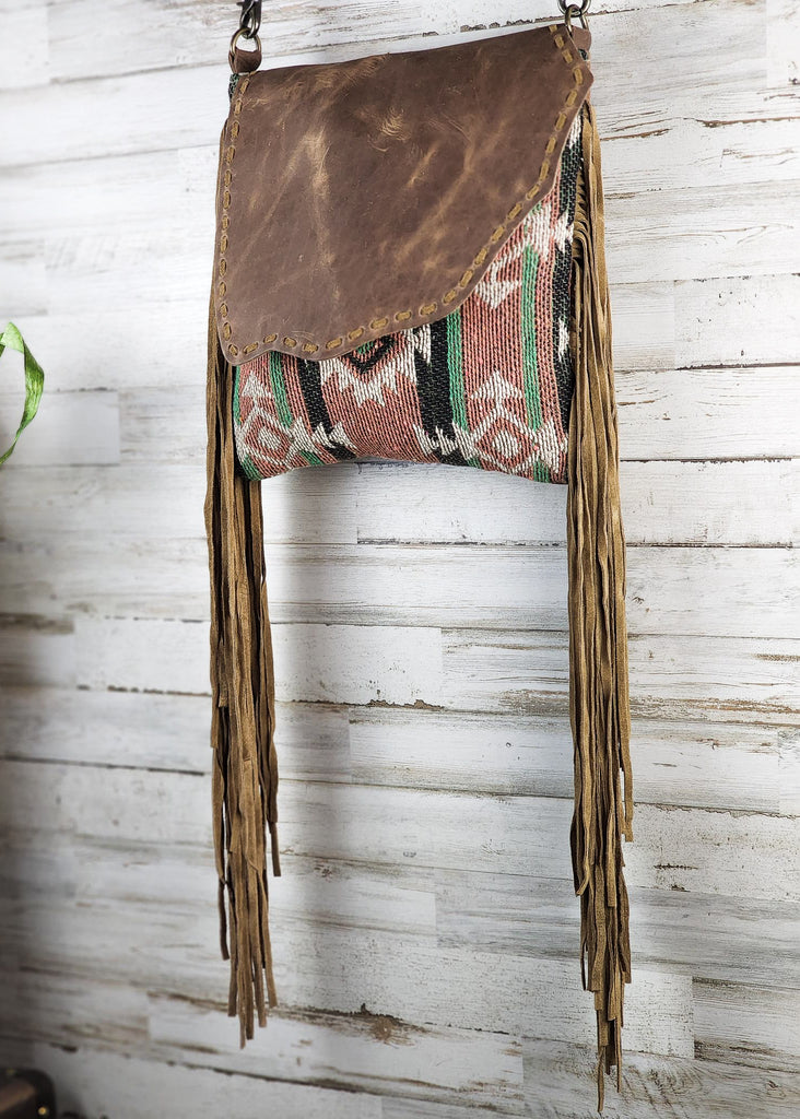 Concealed carry crossbody with leather flap snap with southwestern woven design. Fringe falls from the side of the purse. 
