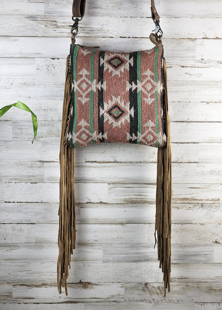 Flap is flipped to the backside showing the Southwestern woven crossbody purse. Fringe hangs from side of bag. 