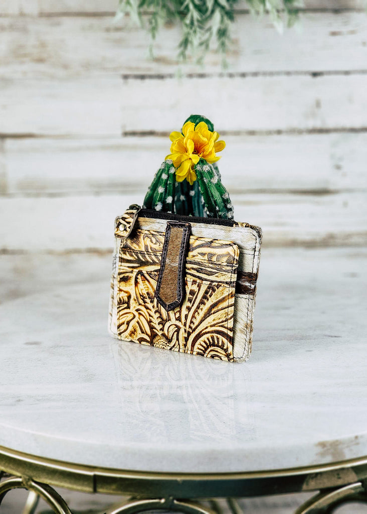 Cowhide Filigree Card Holder with embossed contrast leather design. Card holders can be seen and top zippered pocket. Wallet lays against a cactus put and marble table top.