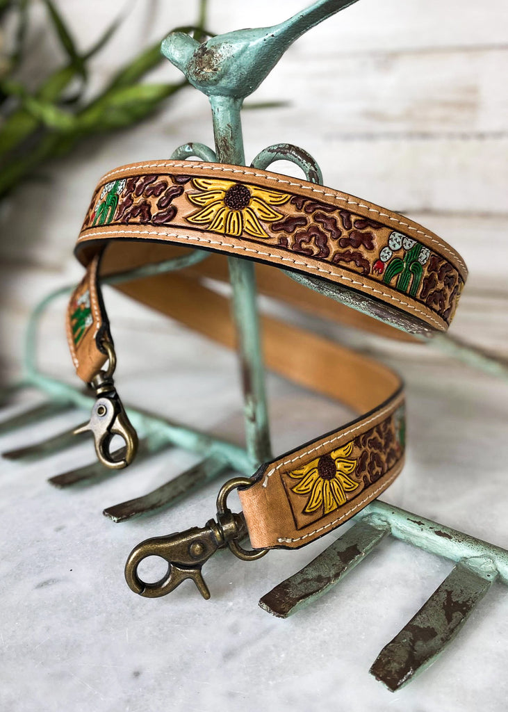 Brown purse strap with sunflowers and cacti detail, taken on white table with green floral décor 