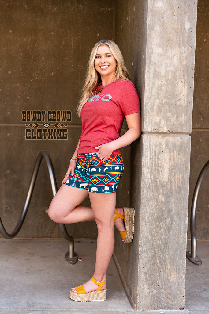 Southwestern buffalo shorts coming to about mid thigh. Pockets are visible. Model wears this with red short sleeve tee with hands in pocket.