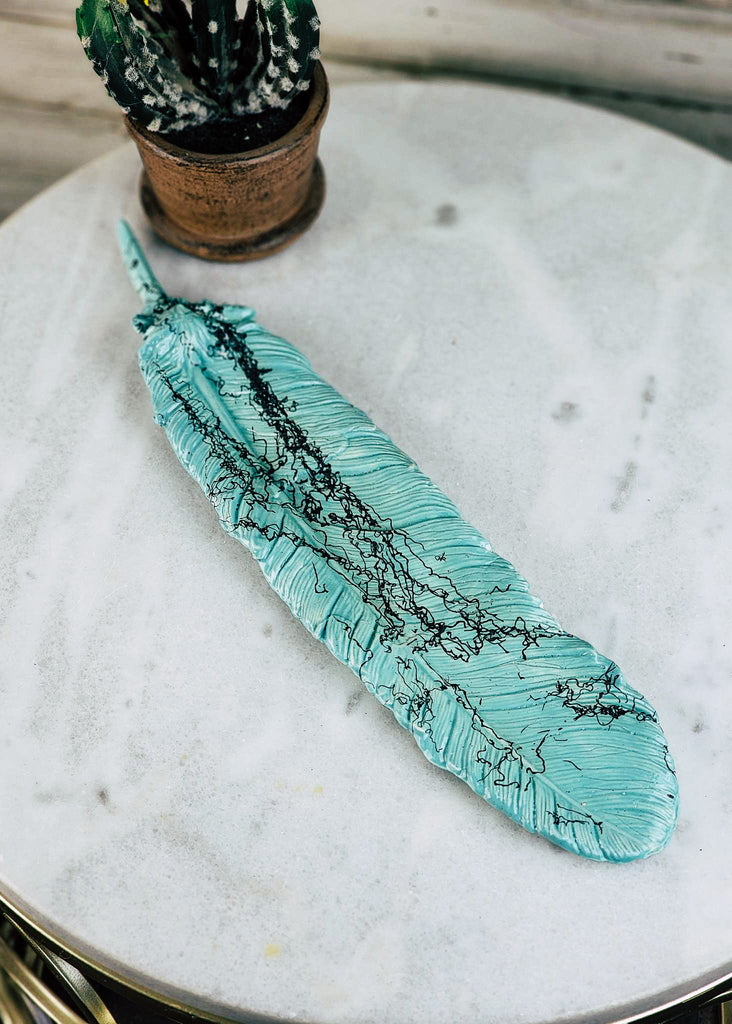 Turquoise feather horse hair pottery decor with textured feather design and black horse hair. Pottery lays on white marble table. 