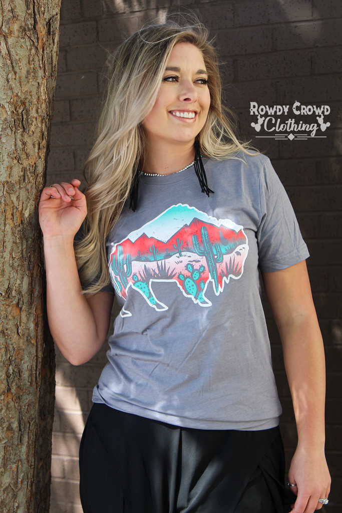 Grey short sleeve with a white outlined background and a desert scene inside of the buffalo. Red and shades of turquoise make up the desert scene (mountains and cacti). 