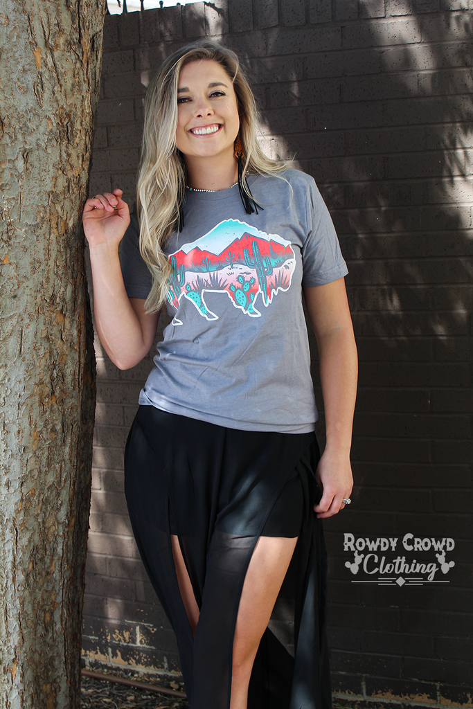 Grey short sleeve with a white outlined background and a desert scene inside of the buffalo. Red and shades of turquoise make up the desert scene (mountains and cacti). 