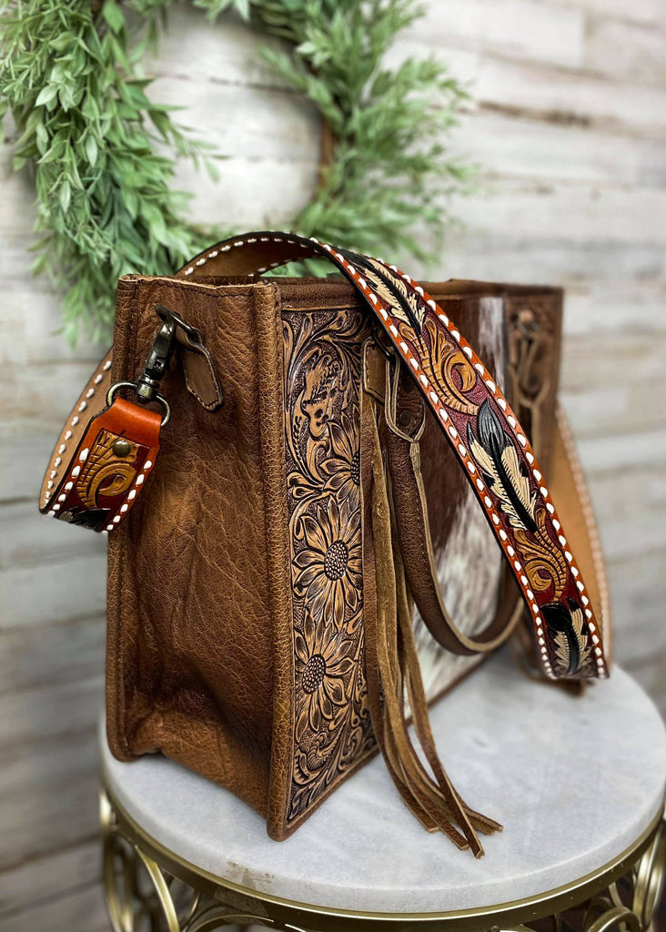 Multi colored purse strap with detailed feather with whipstitched detail, taken inside on brown handbag with floral décor 