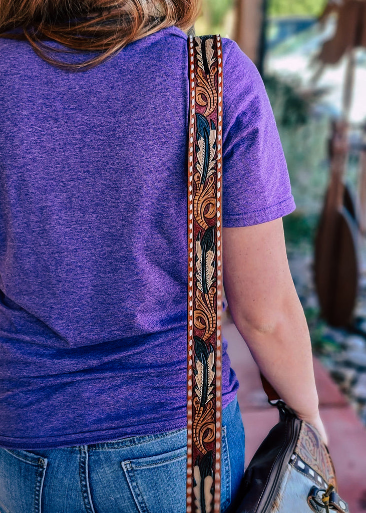 Multi colored purse strap with detailed feather with whipstitched detail, taken outside on model  