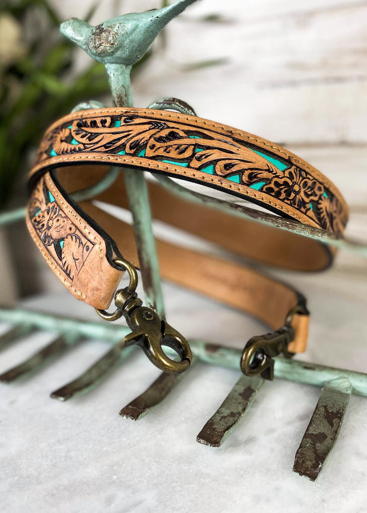 Brown purse strap with floral tooled detail and teal color detail, taken on white table 