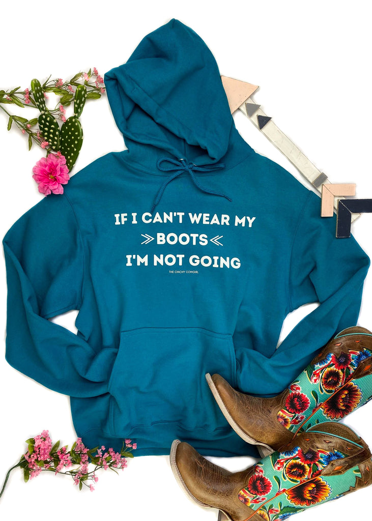 Teal hoodie laid flat on white surface with green and pink floral décor, with "If I Can't Wear My Boots, I'm Not Going" graphic in white ink, in the center of the hoodie 